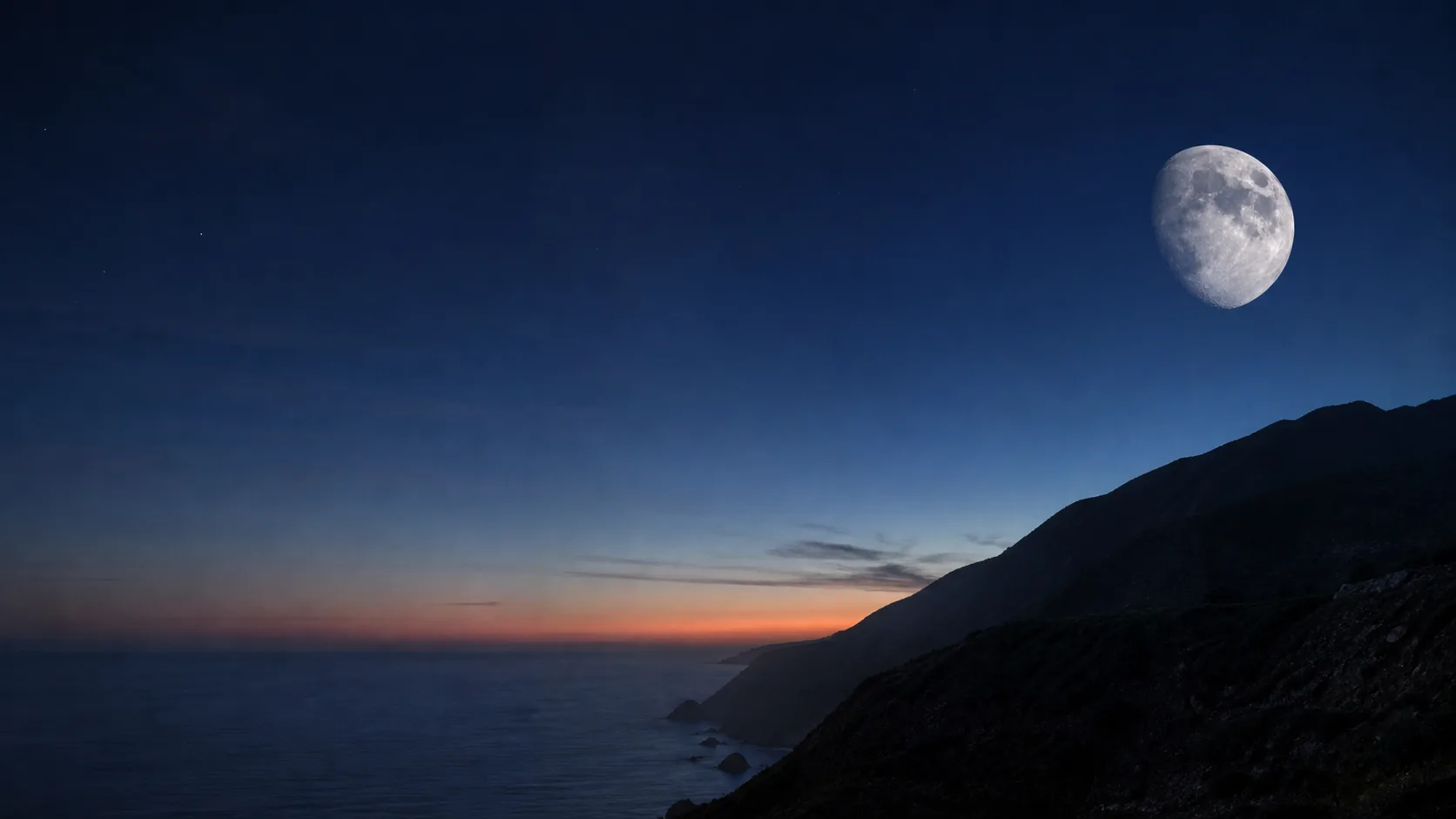 A waxing gibbous Moon above a dark coastal ridge at blue hour.